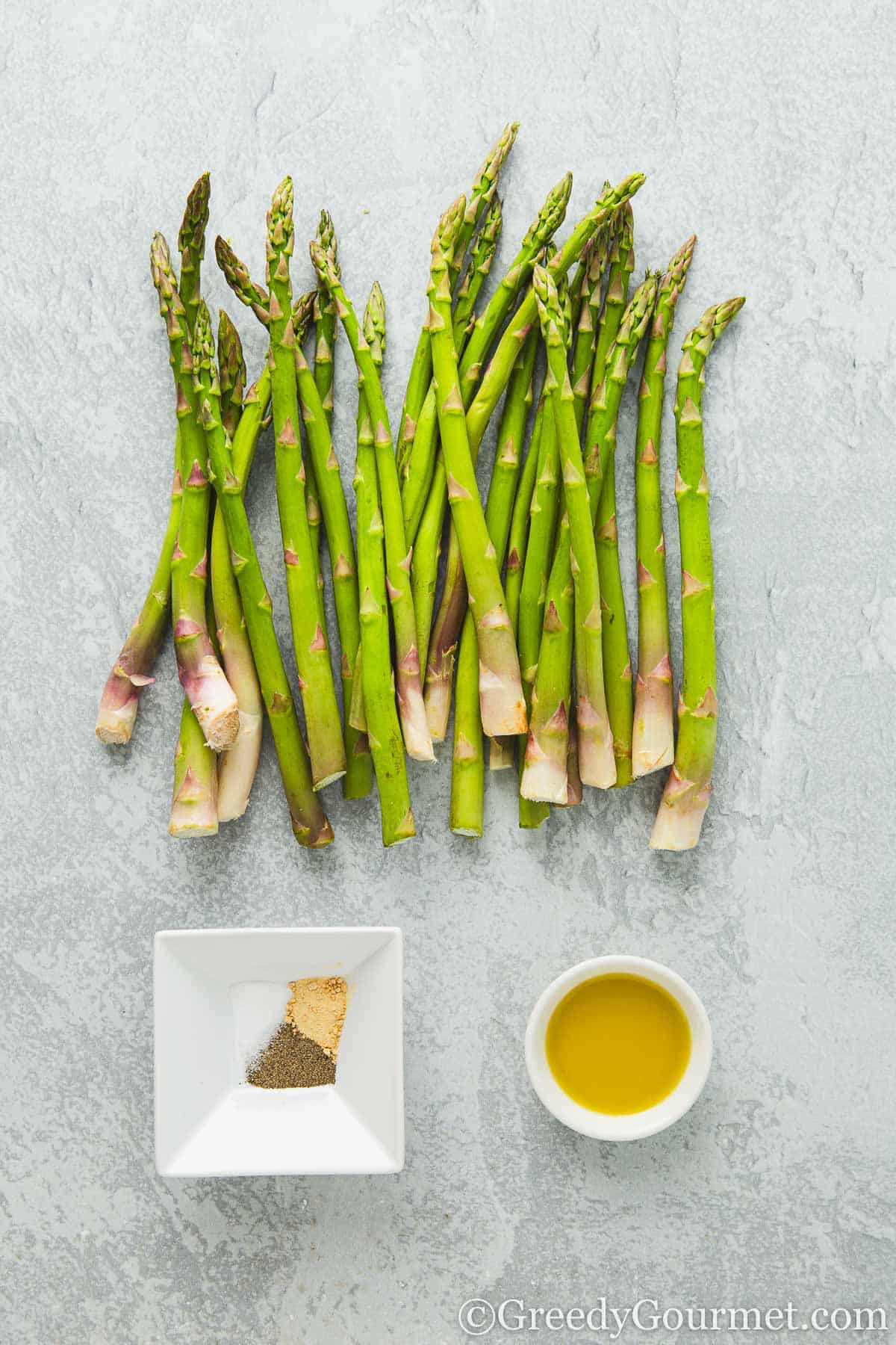 Asparagus next to bowls of seasoning and oil.