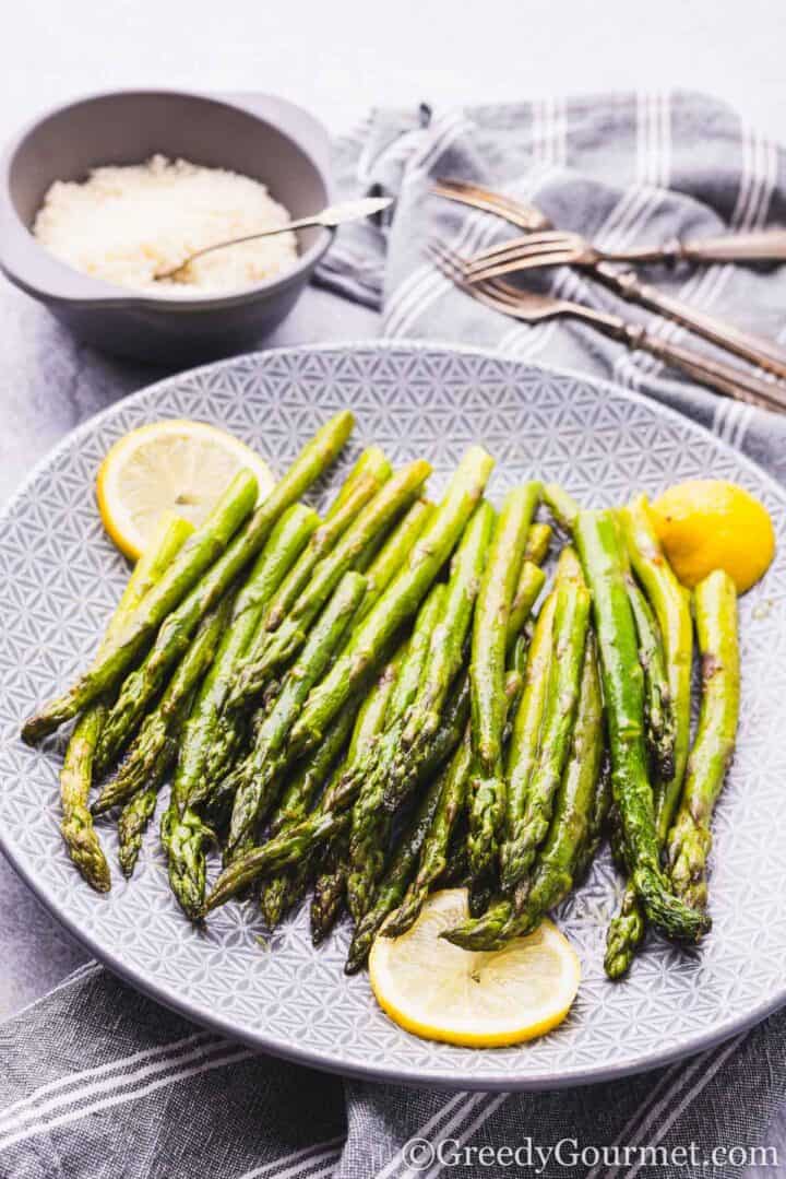 Roasted asparagus on a plate served with lemon slices.