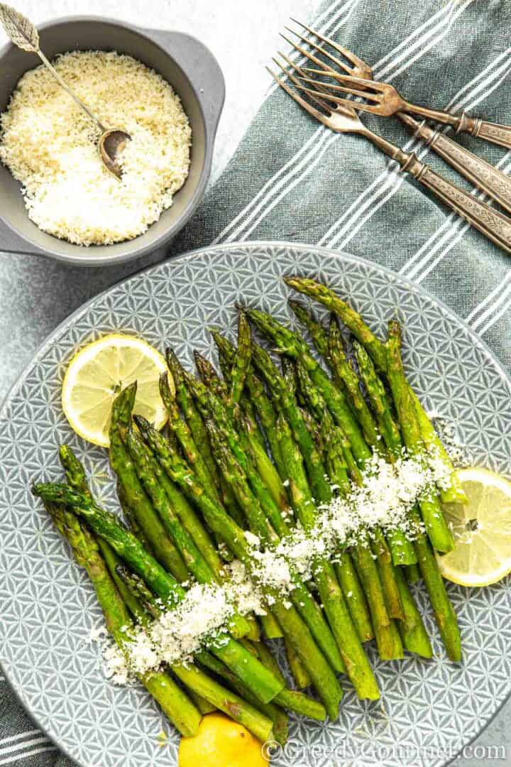 Roasted asparagus on a plate served with lemon slices.